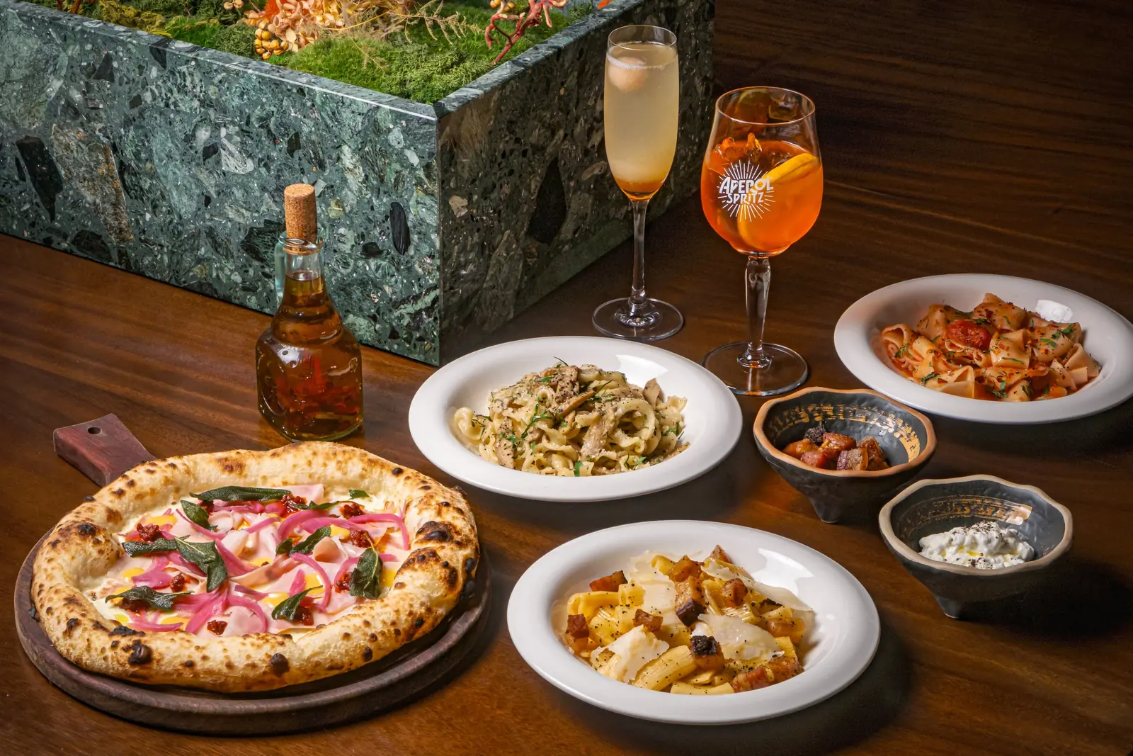 Pizza, pasta, Aperol and a spritz laid out on a dark table at Casa Vostra