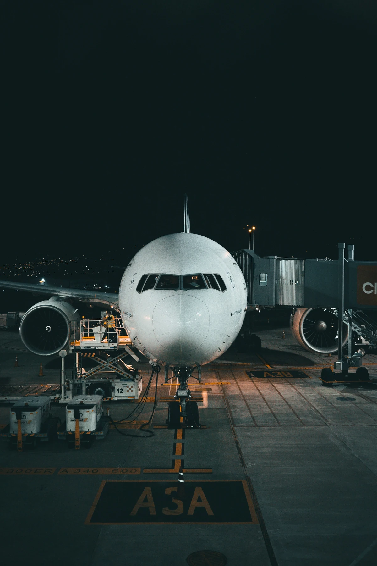 An airliner at the gate at night, with ground crew servicing it