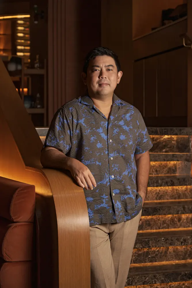 Lim Kian Chun leaning against a curved timber wall beside a lit stone staircase